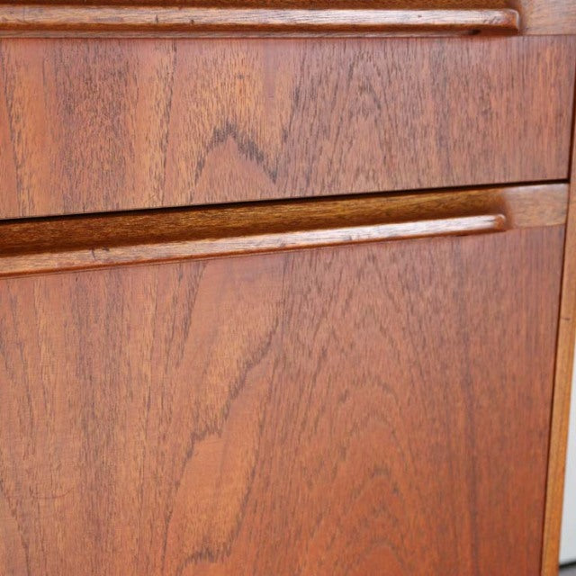 Close-up of vintage teak cabinet door showing rich wood grain and smooth integrated handle, British mid-century design.