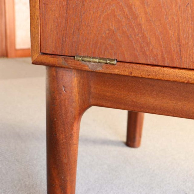 Close-up of vintage teak cabinet leg and lower corner showing rich wood grain, mid-century British design by Macintosh with.