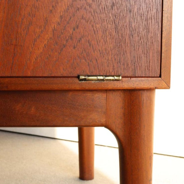 Close-up of vintage British mid-century teak cabinet leg and wood grain with brass hinge detail.