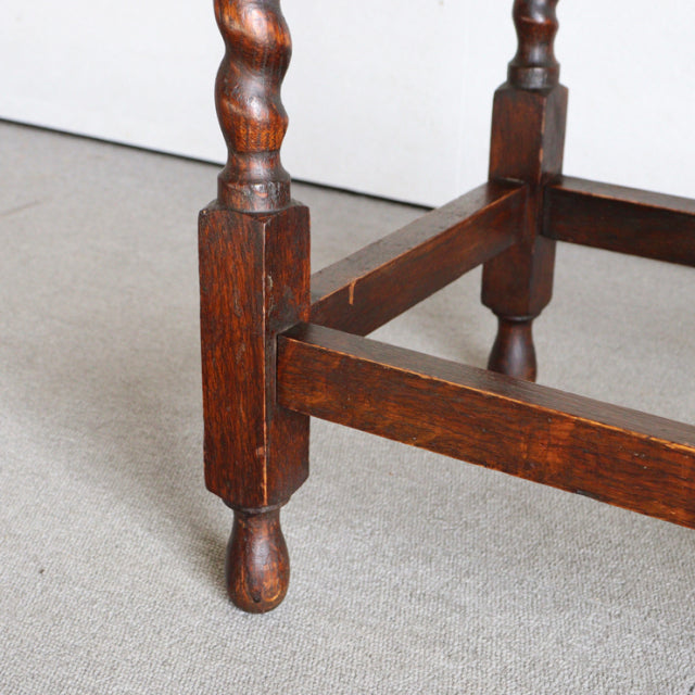 Vintage British mid-century teak side table leg with detailed turned wood grain and sturdy square supports on beige carpet.