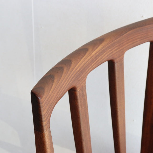 Close-up of vintage teak dining chair backrest with smooth curved top rail and visible wood grain, mid-century British.