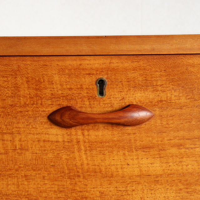 Close-up of vintage teak wood drawer front with smooth grain, elegant curved handle, and keyhole, British mid-century style.