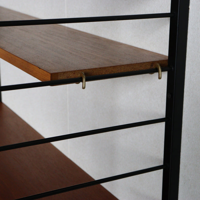 Mid-century British Ladderax shelving unit with teak wood shelves and black metal frame, featuring brass hooks and visible.