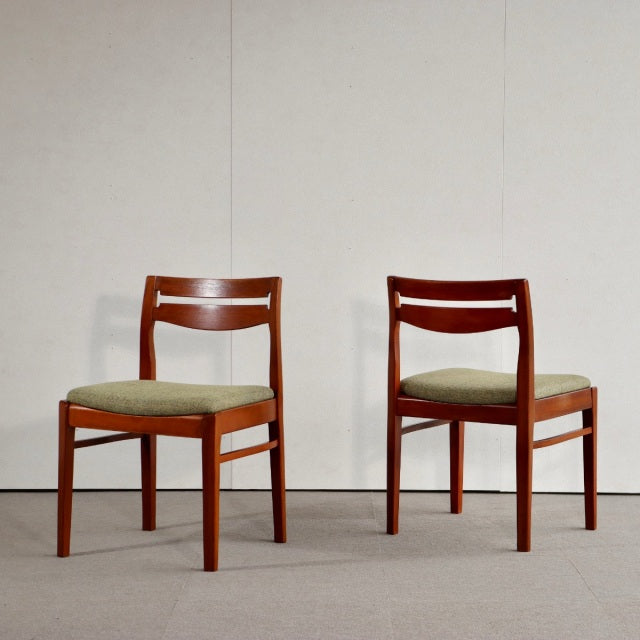 Set of two mid-century British dining chairs in vintage teak with gently curved backrests and beige upholstered seats.