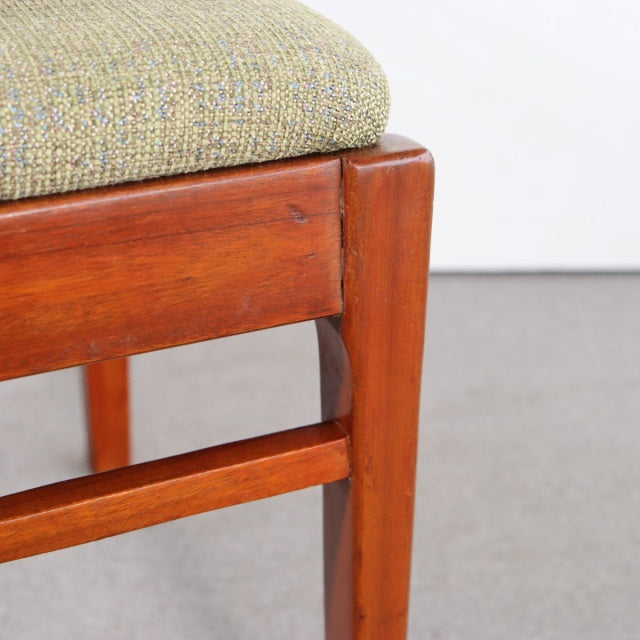 Mid-century teak dining chair leg detail with warm wood grain and light green textured fabric seat, vintage British-Denmark.