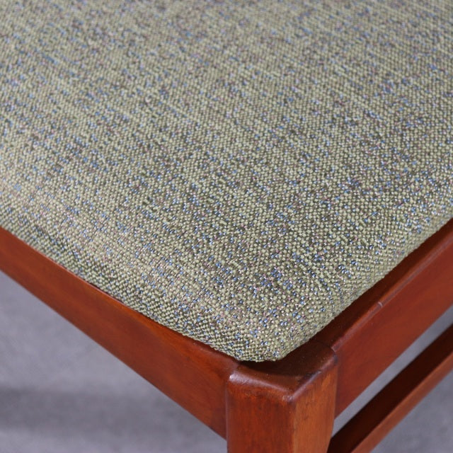 Close-up of vintage teak dining chair seat with textured grayish-green fabric upholstery and visible wood grain on.