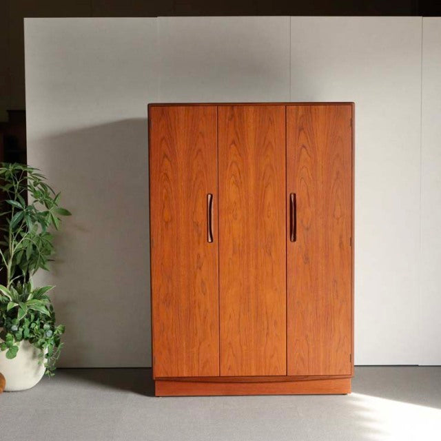 Vintage British mid-century teak wardrobe by G-PLAN with rich wood grain, three doors, and curved wooden handles, standing.