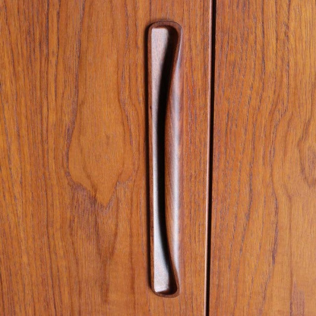 Close-up of vintage British mid-century teak cabinet door with smooth, sculpted wooden handle and rich wood grain from.