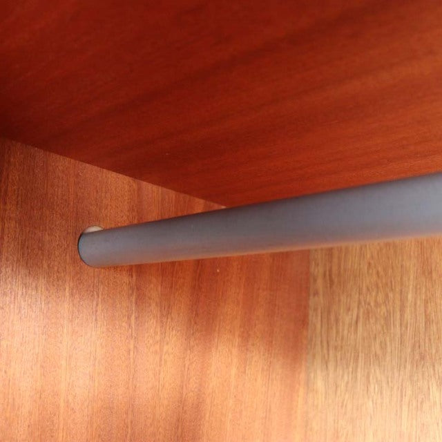 Close-up of vintage British mid-century teak wardrobe corner showing smooth wood grain and grey metal hanging rod detail.