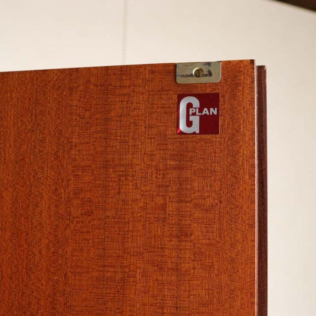 Close-up of mid-century British vintage teak cabinet door featuring G-Plan logo and visible wood grain texture.