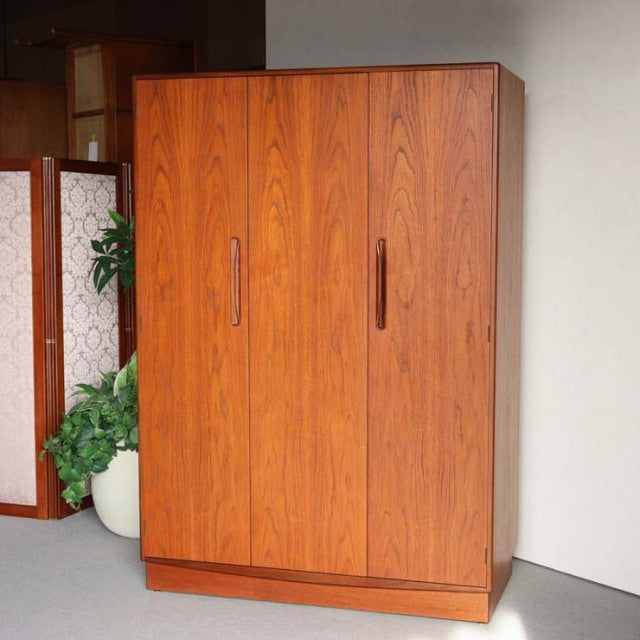 Mid-century British G-Plan teak wardrobe with rich wood grain, vertical handles, and clean lines on solid base legs.