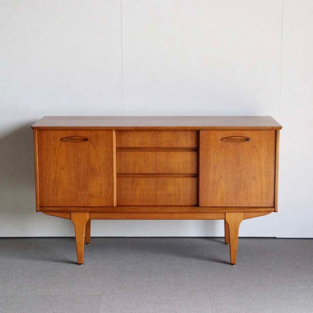 Compact mid-century British teak sideboard by Jentique with rich wood grain, rounded handles, and tapered legs from Denmark.