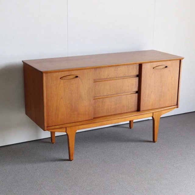 Compact Jentique mid-century British teak sideboard with warm wood grain, tapered legs, and sleek handles.