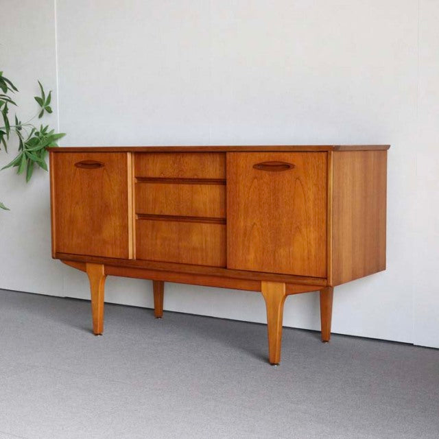 Vintage teak sideboard by Jentique with mid-century British design, sleek wood grain, three central drawers, and tapered.