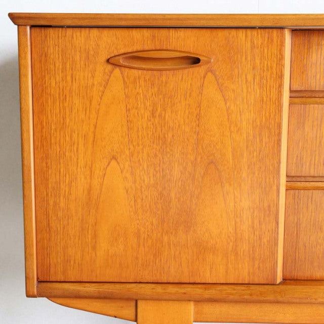 Compact mid-century teak sideboard by Jentique with smooth wood grain, rounded recessed handle, and tapered legs in.
