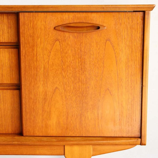 Vintage mid-century teak sideboard by Jentique with smooth wood grain, rounded recessed handle, and tapered legs.