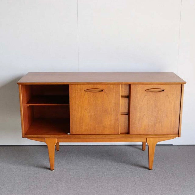 Compact vintage teak sideboard by Jentique, British mid-century design with tapered legs and three doors, natural wood grain .
