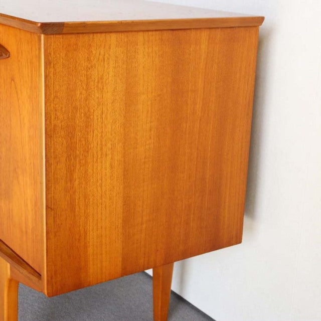 Compact mid-century British teak sideboard by Jentique with sleek wood grain and tapered legs.