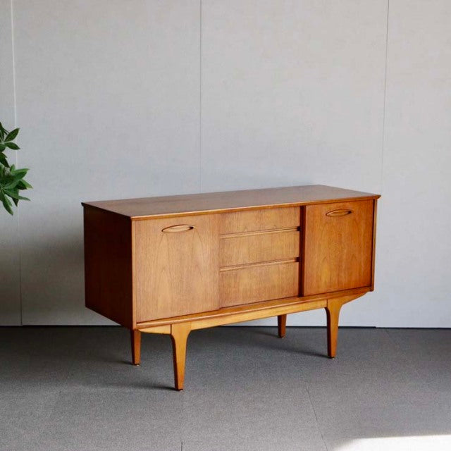 Compact Jentique vintage teak sideboard with mid-century British design, three central drawers, sliding door, and tapered.