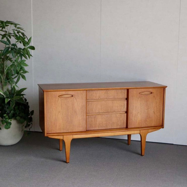 Mid-century British Jentique teak sideboard with smooth wood grain, three central drawers, two cabinet doors, and tapered.