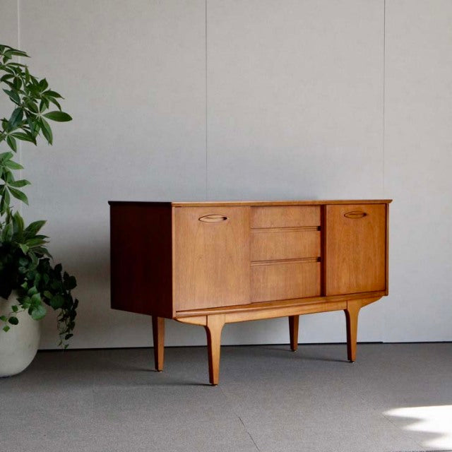 Compact Jentique mid-century British vintage teak sideboard with smooth wood grain, tapered legs, and central drawers.