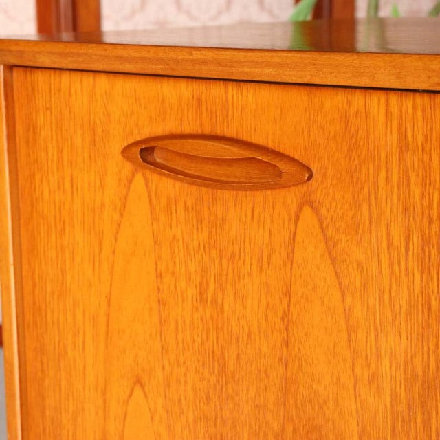 Close-up of vintage Jentique teak sideboard door with sculpted oval recessed handle and warm wood grain from mid-century.