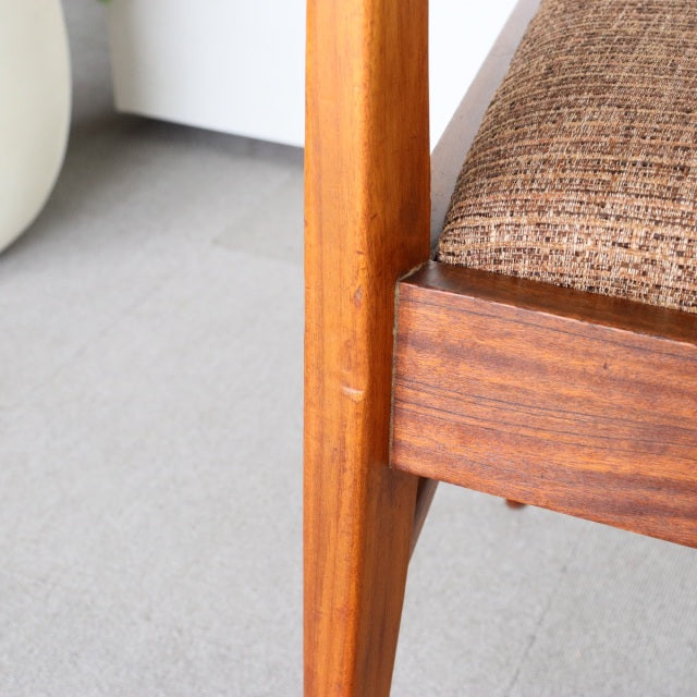 Mid-century British teak dining chair leg and frame with rich wood grain and textured brown seat cushion.
