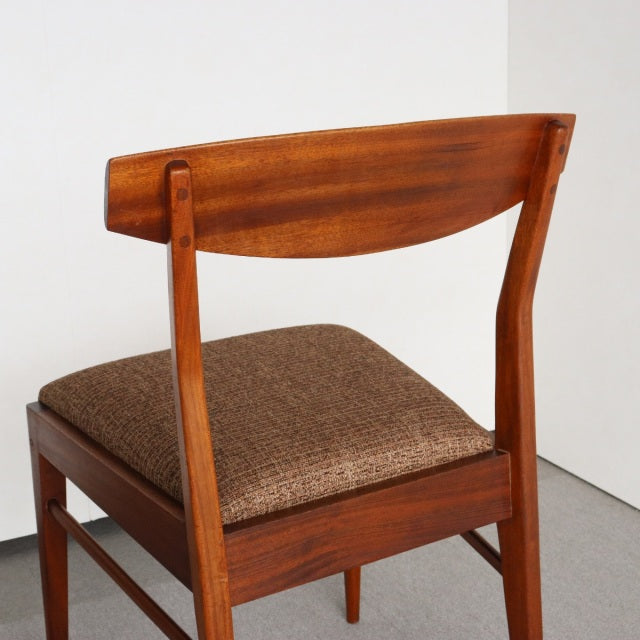 Vintage mid-century McIntosh dining chair in warm teak with visible wood grain, angled backrest, and textured brown fabric.
