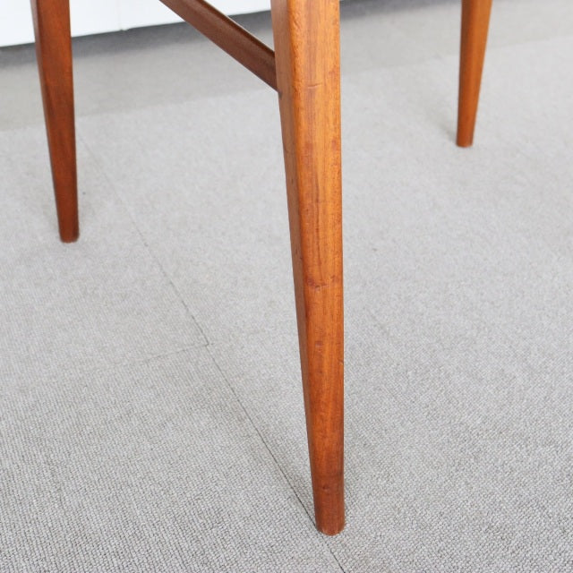 Mid-century British vintage teak dining chair leg with straight grain and tapered design on beige carpet.
