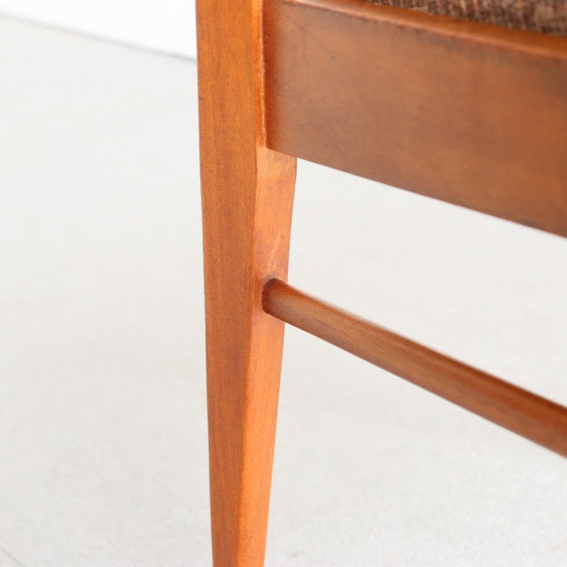 Close-up of vintage mid-century teak dining chair leg with visible wood grain and smooth British design elements.
