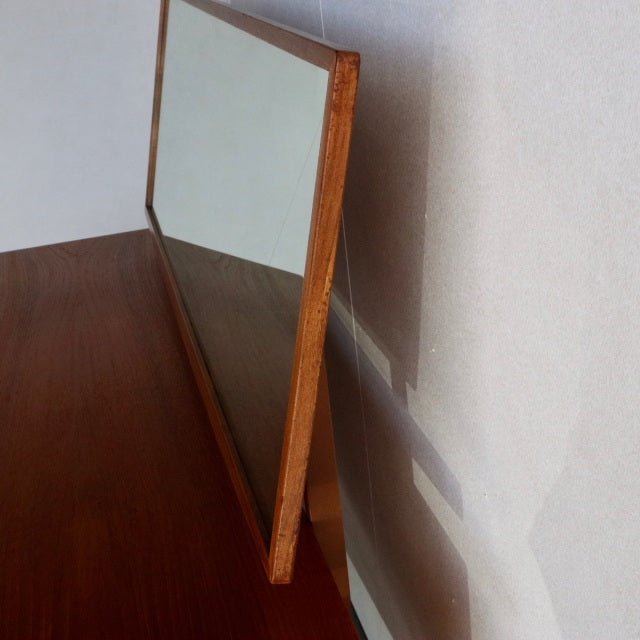 Mid-century British G-PLAN teak dresser mirror with rich wood grain and slender frame, angled against wall.