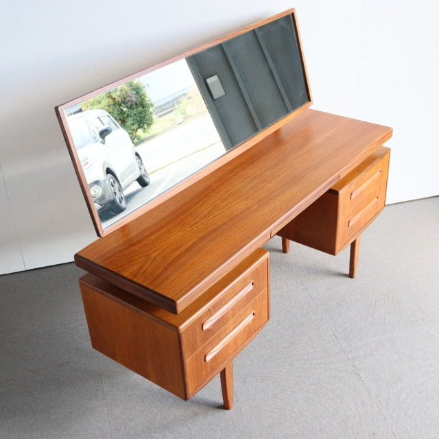 Mid-century British G-Plan teak dresser with rich wood grain, angled rectangular mirror, and tapered legs.