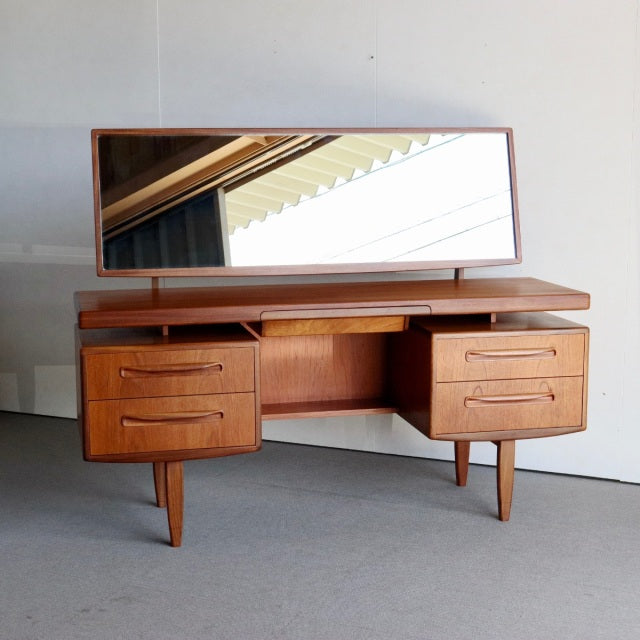 Vintage mid-century G-PLAN teak dresser with wide rectangular mirror, curved drawer handles, and tapered legs, showcasing.