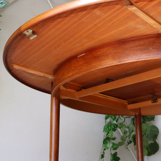 Vintage teak G-Plan dining table underside showing smooth wood grain, rounded edges, and slender mid-century British legs.
