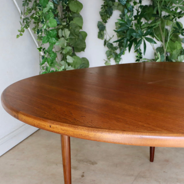 Vintage G-Plan teak dining table with rounded edges and slender mid-century British legs, showing rich wood grain.