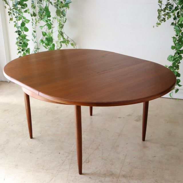 Mid-century British G-Plan vintage teak dining table with oval top and slender tapered legs, rich wood grain visible.