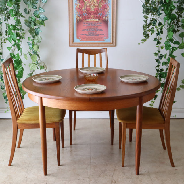 Vintage British mid-century teak dining table with smooth round top and tapered legs, paired with matching teak chairs with.