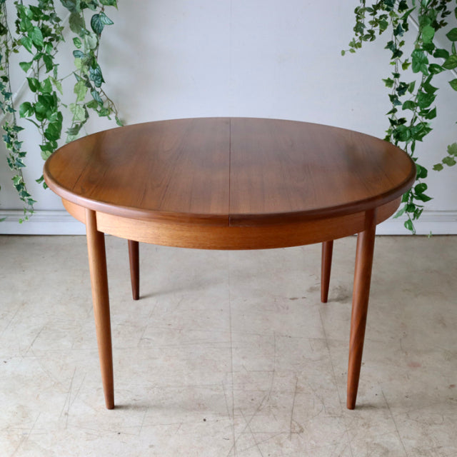 Vintage G-Plan teak dining table with smooth round top, slender tapered legs, mid-century British Denmark design.