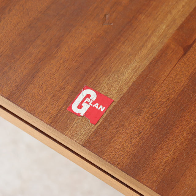 Close-up of vintage teak G-Plan dining table surface showing rich wood grain and brand label on mid-century British.