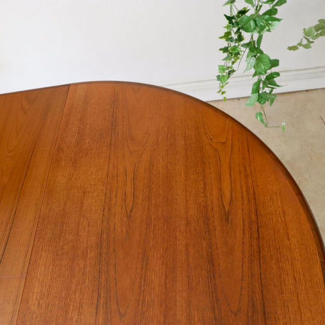 Oval vintage teak dining table with smooth grain, rounded edges, and slender British mid-century legs.