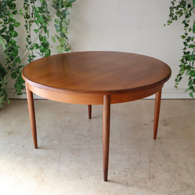 Vintage British teak dining table by G-Plan with smooth round top, tapered mid-century legs, and rich wood grain details,.