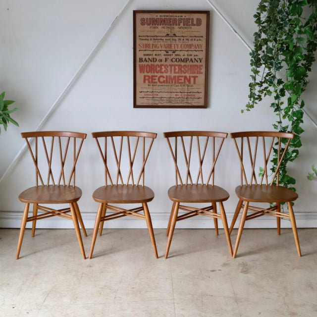Set of four vintage British mid-century teak Ercol X-Back dining chairs with spindle backs and splayed legs.