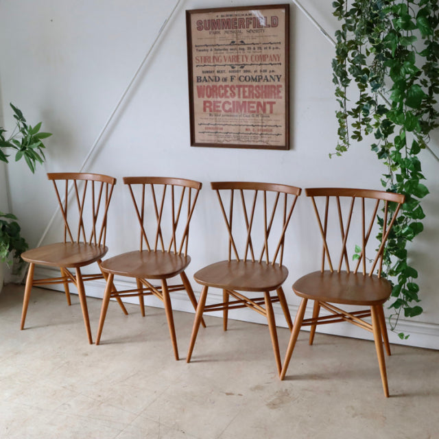 Set of four vintage mid-century British Ercol X-back dining chairs in teak wood with visible grain and slender tapered legs.