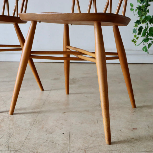Mid-century British Ercol X-Back chair in natural teak with smooth tapered legs and visible wood grain.