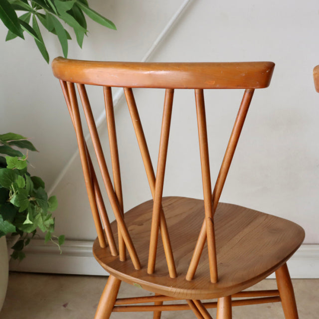 Vintage mid-century British Ercol X-back dining chair in warm teak with visible wood grain and slender angled legs.