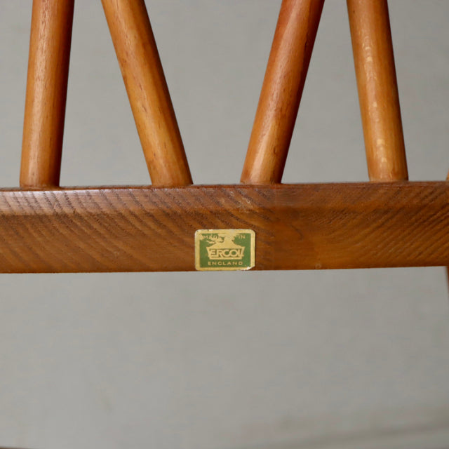 Vintage teak wood X-back chair leg detail with British Ercol brand label and smooth wood grain.