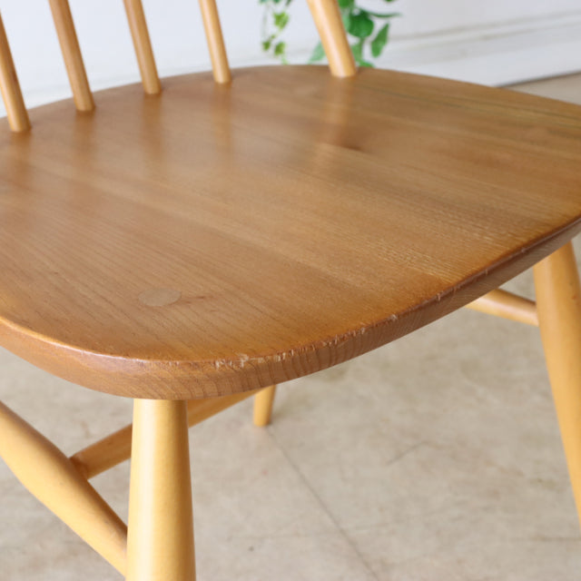 Vintage British mid-century Ercol Quaker chair in teak with smooth curved seat and slender rounded legs showing natural wood .