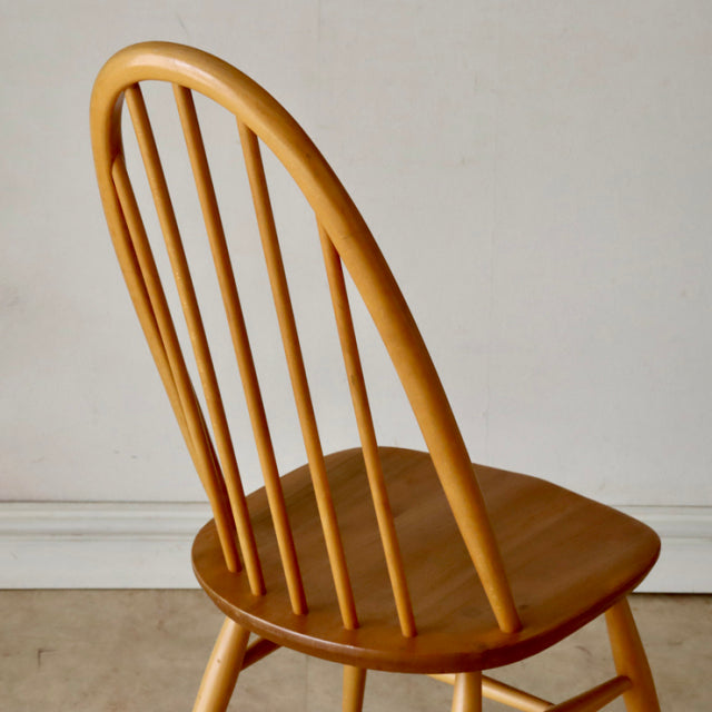 Vintage British mid-century Ercol Quaker chair in light teak with curved spindle back and smooth wood grain seat.