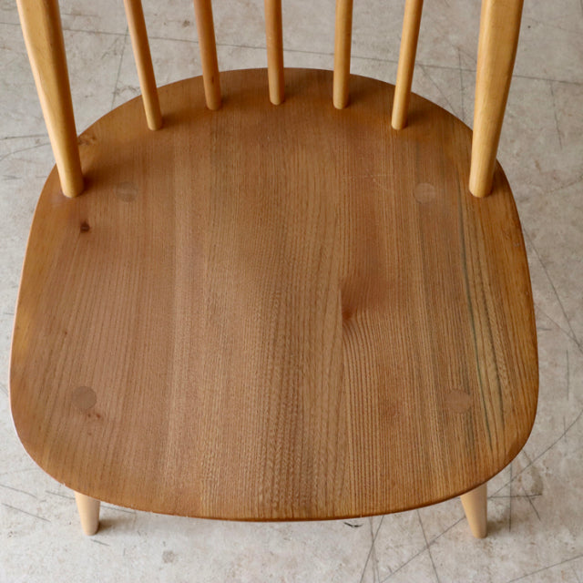 Vintage mid-century British ERCOL Quaker chair in teak with smooth rounded seat, elegant wood grain, and slender spindle.