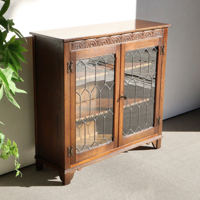 Vintage teak Jaycee mid-century British cabinet with decorative carved top panel and leaded glass doors on short tapered legs.
